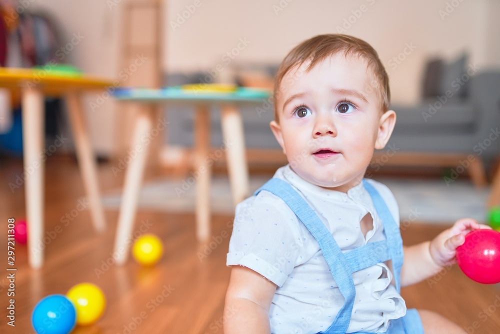 Beautiful toddler sitting on the floor playing with small colorful balls at kindergarten Beautiful toddler sitting on the floor playing with small colorful balls at kindergarten