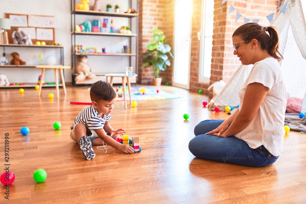 Fototapeta premium Beautiful teacher and toddler boy playing with train at kindergarten