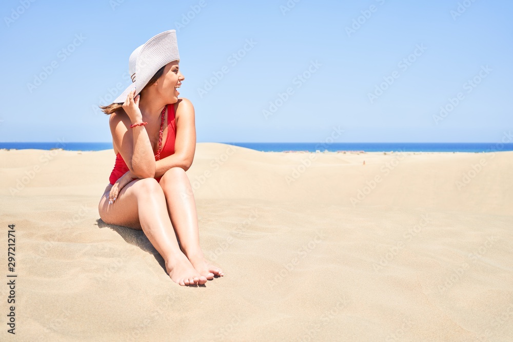 Young beautiful woman sunbathing sitting on the sand wearing summer swinsuit at maspalomas dunes bech Young beautiful woman sunbathing sitting on the sand wearing summer swinsuit at maspalomas dunes bech