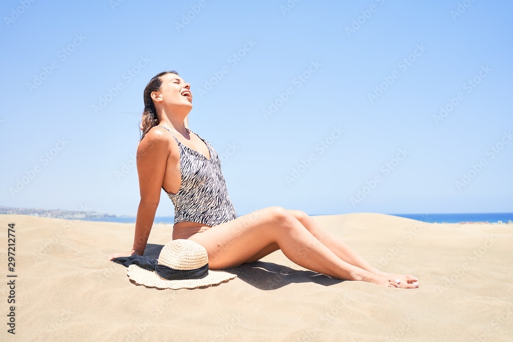 Young beautiful woman sunbathing sitting on the sand wearing summer swinsuit at maspalomas dunes bech Young beautiful woman sunbathing sitting on the sand wearing summer swinsuit at maspalomas dunes bech