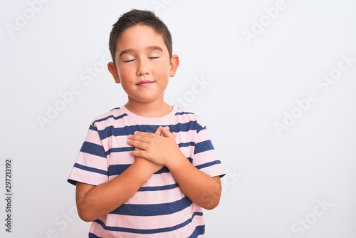 Beautiful kid boy wearing casual striped t-shirt standing over isolated white background smiling with hands on chest with closed eyes and grateful gesture on face. Health concept.