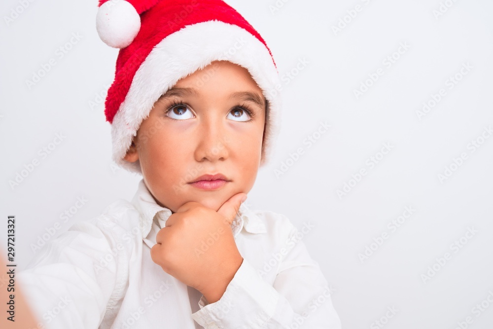 Beautiful kid boy wearing Christmas Santa hat make selfie over isolated white background serious face thinking about question, very confused idea Beautiful kid boy wearing Christmas Santa hat make selfie over isolated white background serious face thinking about question, very confused idea
