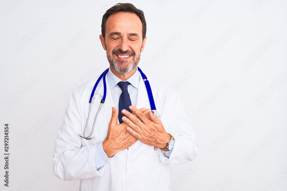 Middle age doctor man wearing coat and stethoscope standing over isolated white background smiling with hands on chest with closed eyes and grateful gesture on face. Health concept. Middle age doctor man wearing coat and stethoscope standing over isolated white background smiling with hands on chest with closed eyes and grateful gesture on face. Health concept.