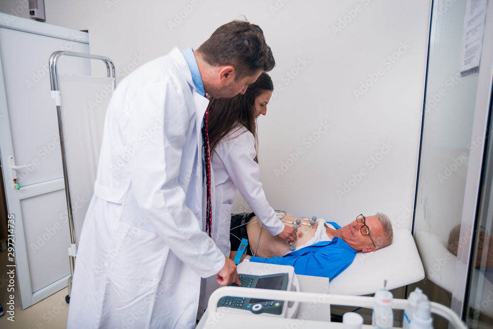 Obraz premium Doctor ( cardiologist ) is attaching vacuum sensors to an elder ( senior )patient for recording ECG or EKG cardiogram test..