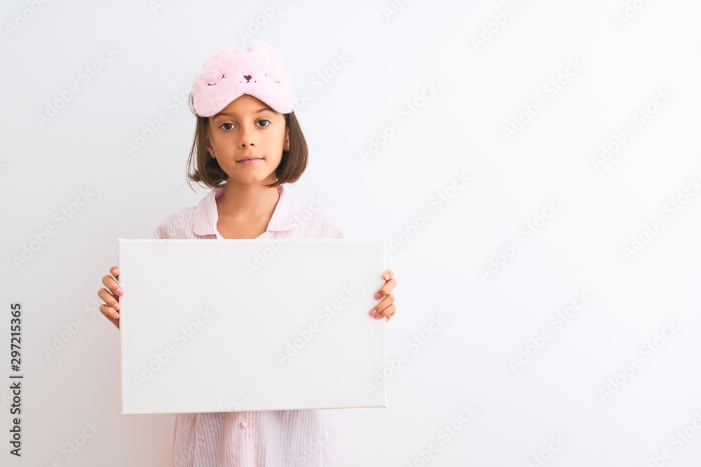 Child girl wearing sleep mask and pajama holding banner over isolated white background with a confident expression on smart face thinking serious Child girl wearing sleep mask and pajama holding banner over isolated white background with a confident expression on smart face thinking serious