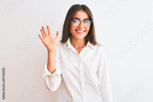 Young beautiful businesswoman wearing glasses standing over isolated white background Waiving saying hello happy and smiling, friendly welcome gesture