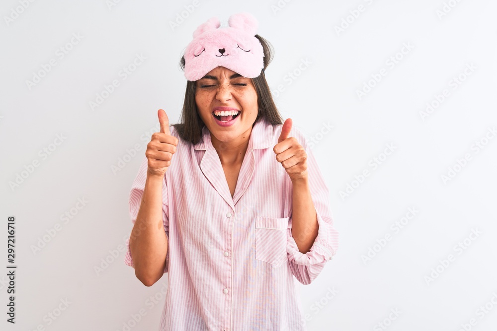 Young beautiful woman wearing sleep mask and pajama over isolated white background excited for success with arms raised and eyes closed celebrating victory smiling. Winner concept. Young beautiful woman wearing sleep mask and pajama over isolated white background excited for success with arms raised and eyes closed celebrating victory smiling. Winner concept.