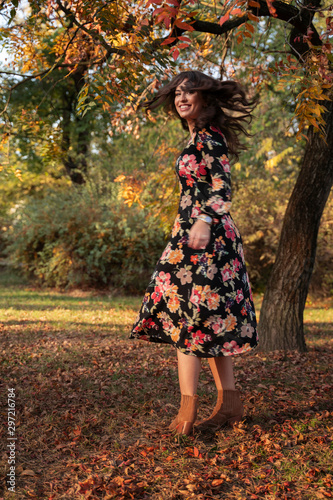 Cheerful stylish girl in floral dress spinning in the park  autumn season 