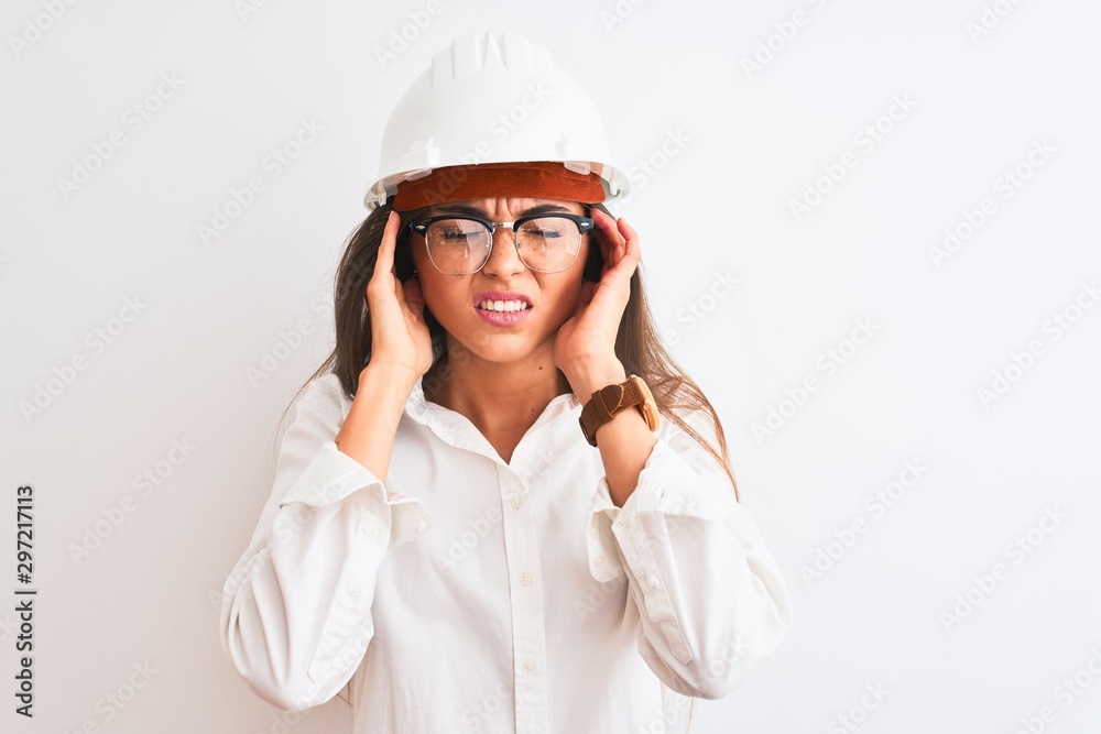 Young beautiful architect woman wearing helmet and glasses over isolated white background with hand on head for pain in head because stress. Suffering migraine. Young beautiful architect woman wearing helmet and glasses over isolated white background with hand on head for pain in head because stress. Suffering migraine.