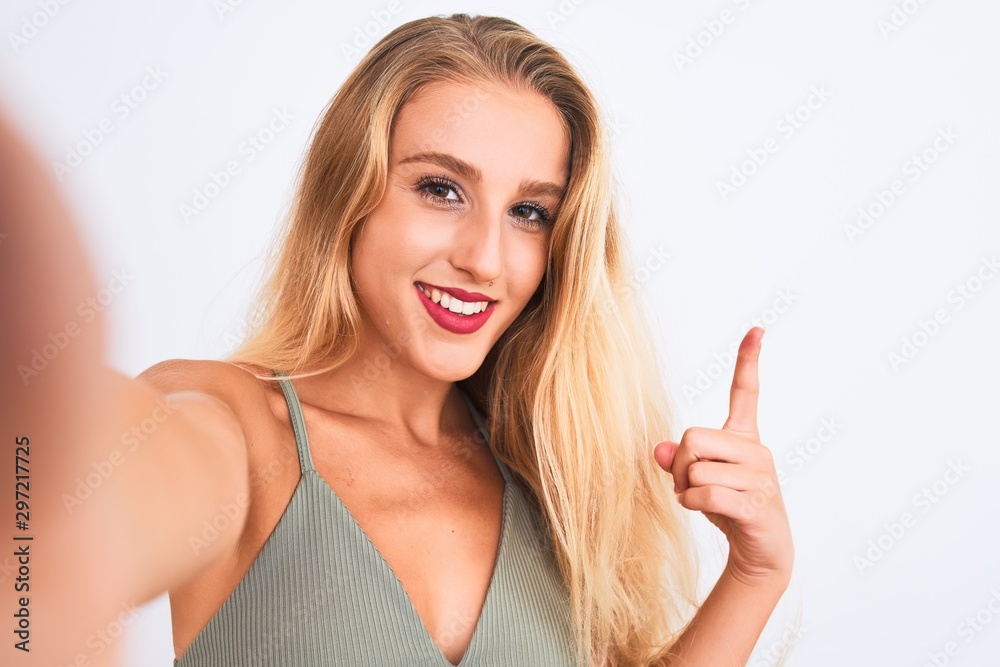 Young beautiful woman wearing t-shirt make selfie by camera over isolated white background surprised with an idea or question pointing finger with happy face, number one Young beautiful woman wearing t-shirt make selfie by camera over isolated white background surprised with an idea or question pointing finger with happy face, number one