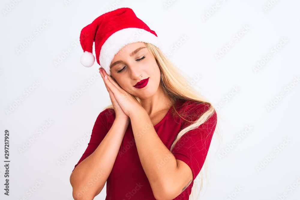 Young beautiful woman wearing Christmas Santa hat over isolated white background sleeping tired dreaming and posing with hands together while smiling with closed eyes. Young beautiful woman wearing Christmas Santa hat over isolated white background sleeping tired dreaming and posing with hands together while smiling with closed eyes.