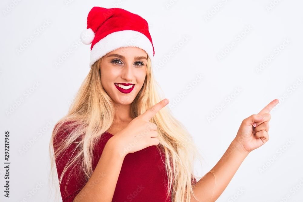 Young beautiful woman wearing Christmas Santa hat over isolated white background smiling and looking at the camera pointing with two hands and fingers to the side.