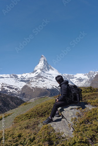 a man with backpack sitting on rock with Matterhorn mountain view in Switzerland. Travel lifestyle and adventurous