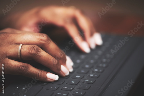 Isolated close-up of ethnic hands typing on black keyboard with white letters on wooden table