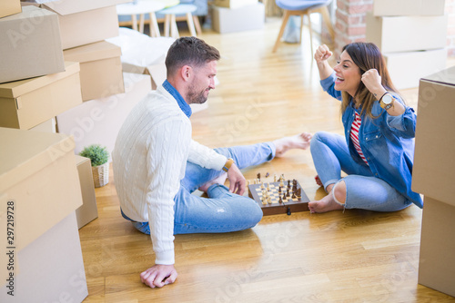 Young beautiful couple playing chess at new home around cardboard boxes