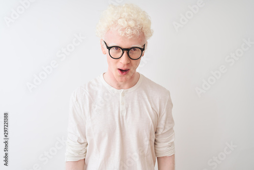 Young albino blond man wearing t-shirt and glasses standing over isolated white background afraid and shocked with surprise expression, fear and excited face.