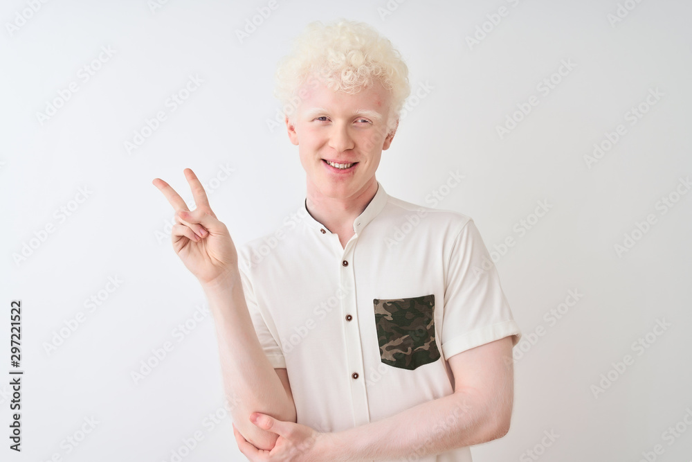 Young albino blond man wearing casual shirt standing over isolated white background smiling with happy face winking at the camera doing victory sign. Number two.