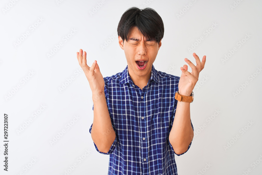Young chinese man wearing casual blue shirt standing over isolated white background celebrating mad and crazy for success with arms raised and closed eyes screaming excited. Winner concept Young chinese man wearing casual blue shirt standing over isolated white background celebrating mad and crazy for success with arms raised and closed eyes screaming excited. Winner concept