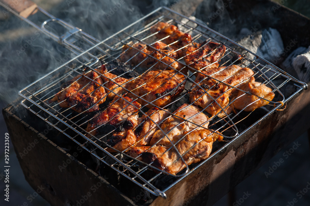 Close-up on the process of cooking shashlik of pork or beef meat clamped in a grill with a crispy burnt crust over gray burnt coals on an open fire with smoke going up.