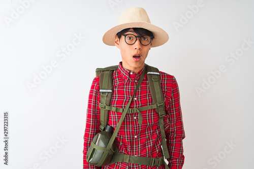 Chinese hiker man wearing backpack canteen glasses hat over isolated white background afraid and shocked with surprise expression, fear and excited face.