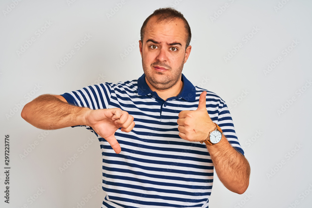 Young man wearing casual striped polo standing over isolated white background Doing thumbs up and down, disagreement and agreement expression. Crazy conflict Young man wearing casual striped polo standing over isolated white background Doing thumbs up and down, disagreement and agreement expression. Crazy conflict