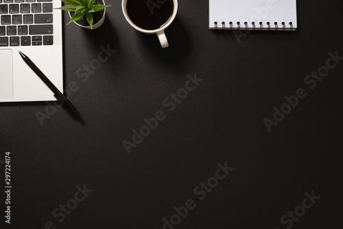 desk office top view with computer, notepad, pen, coffee and plant on black background. flat lay with copy space.