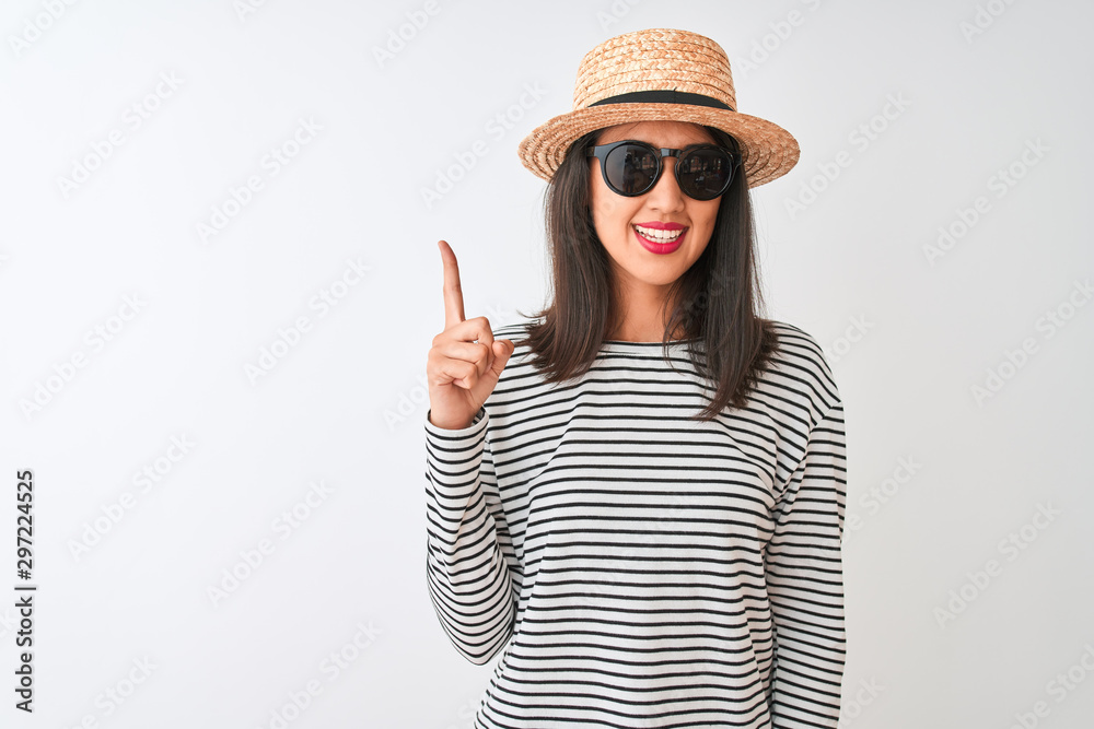 Chinese woman wearing striped t-shirt hat sunglasses standing over isolated white background pointing finger up with successful idea. Exited and happy. Number one. Chinese woman wearing striped t-shirt hat sunglasses standing over isolated white background pointing finger up with successful idea. Exited and happy. Number one.