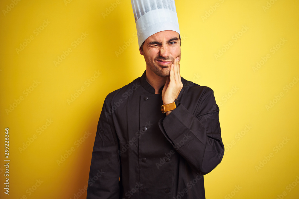 Young chef man wearing uniform and hat standing over isolated yellow background touching mouth with hand with painful expression because of toothache or dental illness on teeth. Dentist concept. Young chef man wearing uniform and hat standing over isolated yellow background touching mouth with hand with painful expression because of toothache or dental illness on teeth. Dentist concept.