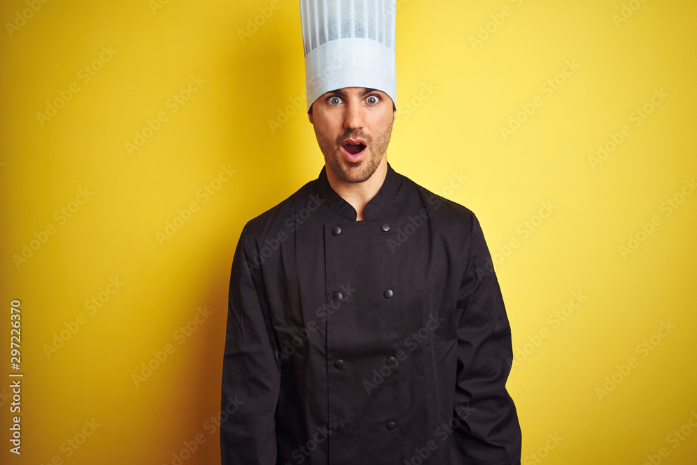 Young chef man wearing uniform and hat standing over isolated yellow background afraid and shocked with surprise expression, fear and excited face. Young chef man wearing uniform and hat standing over isolated yellow background afraid and shocked with surprise expression, fear and excited face.
