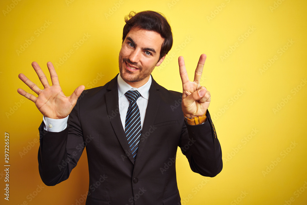Young handsome businessman wearing suit and tie standing over isolated yellow background showing and pointing up with fingers number seven while smiling confident and happy. Young handsome businessman wearing suit and tie standing over isolated yellow background showing and pointing up with fingers number seven while smiling confident and happy.