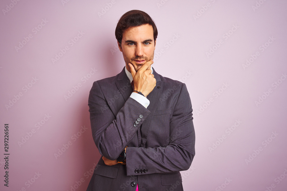 Young handsome businessman wearing suit and tie standing over isolated pink background looking confident at the camera with smile with crossed arms and hand raised on chin. Thinking positive. Young handsome businessman wearing suit and tie standing over isolated pink background looking confident at the camera with smile with crossed arms and hand raised on chin. Thinking positive.