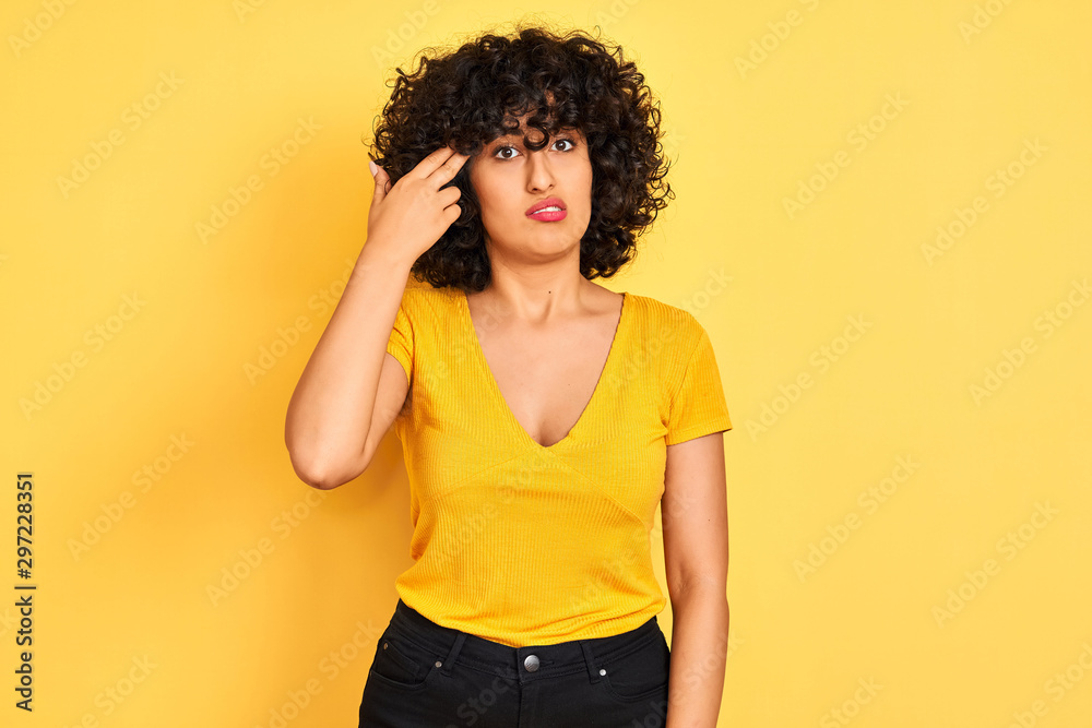 Young arab woman with curly hair wearing t-shirt standing over isolated yellow background Shooting and killing oneself pointing hand and fingers to head like gun, suicide gesture. Young arab woman with curly hair wearing t-shirt standing over isolated yellow background Shooting and killing oneself pointing hand and fingers to head like gun, suicide gesture.