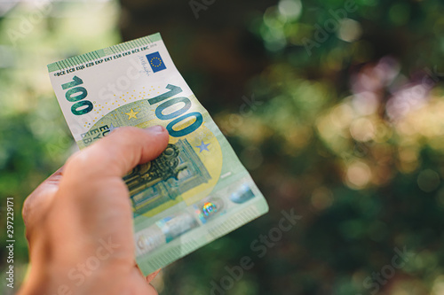 Male hand holding 100 hundredth euro banknote on green background photo