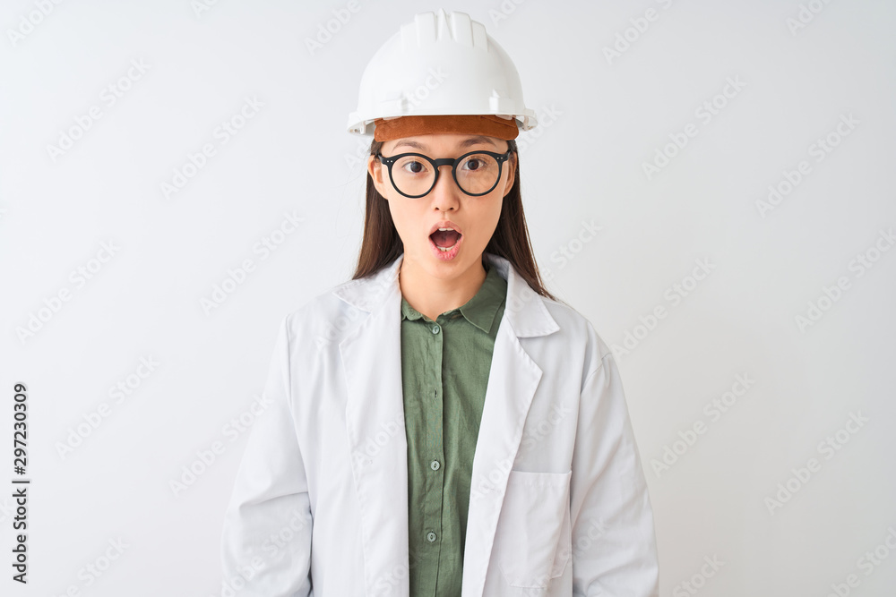 Young chinese engineer woman wearing coat helmet glasses over isolated white background afraid and shocked with surprise expression, fear and excited face. Young chinese engineer woman wearing coat helmet glasses over isolated white background afraid and shocked with surprise expression, fear and excited face.