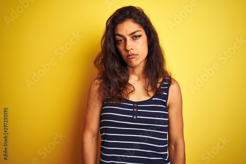 Young beautiful woman wearing striped t-shirt standing over isolated yellow background looking sleepy and tired, exhausted for fatigue and hangover, lazy eyes in the morning.