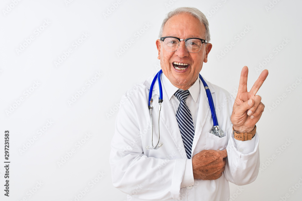 Senior grey-haired doctor man wearing stethoscope standing over isolated white background smiling with happy face winking at the camera doing victory sign. Number two. Senior grey-haired doctor man wearing stethoscope standing over isolated white background smiling with happy face winking at the camera doing victory sign. Number two.