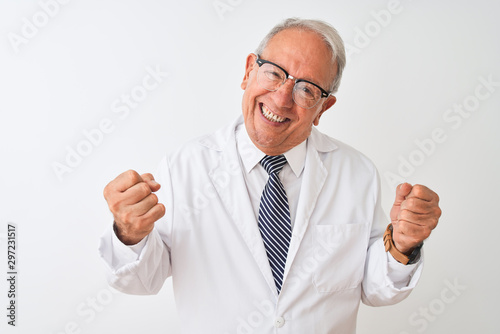 Senior grey-haired scientist man wearing coat standing over isolated white background very happy and excited doing winner gesture with arms raised, smiling and screaming for success