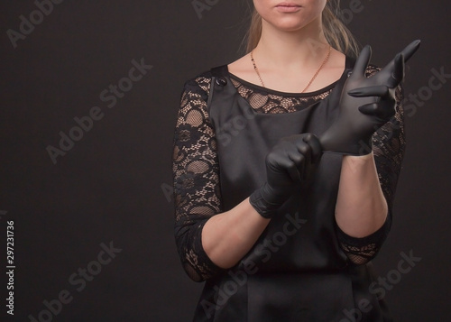 A woman in a black dress with gloves poses in the Studio on a dark background, posing with her hands.