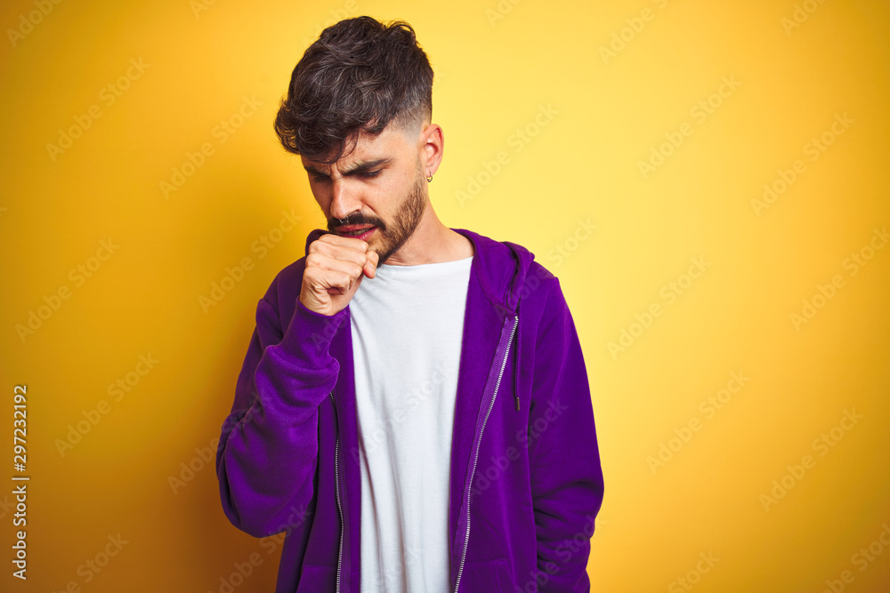 Young man with tattoo wearing sport purple sweatshirt over isolated yellow background feeling unwell and coughing as symptom for cold or bronchitis. Healthcare concept. Young man with tattoo wearing sport purple sweatshirt over isolated yellow background feeling unwell and coughing as symptom for cold or bronchitis. Healthcare concept.
