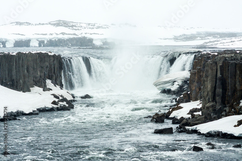 Selfoss waterfall (part of Jökulsá á Fjöllum river in the north of Iceland originating from Vatnajokull glacier) in winter, pictured with snow icicles, snow patterns and spray over the stream 