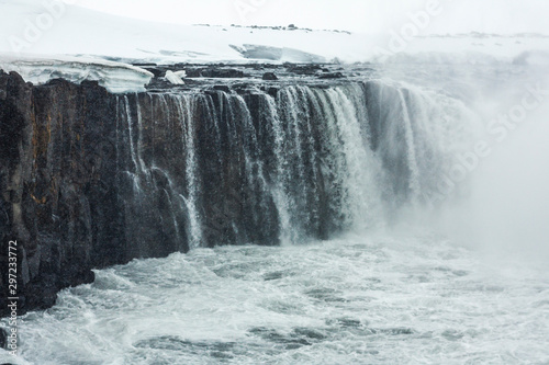 Selfoss waterfall (part of Jökulsá á Fjöllum river in the north of Iceland originating from Vatnajokull glacier) in winter, pictured with snow icicles, snow patterns and spray over the stream 