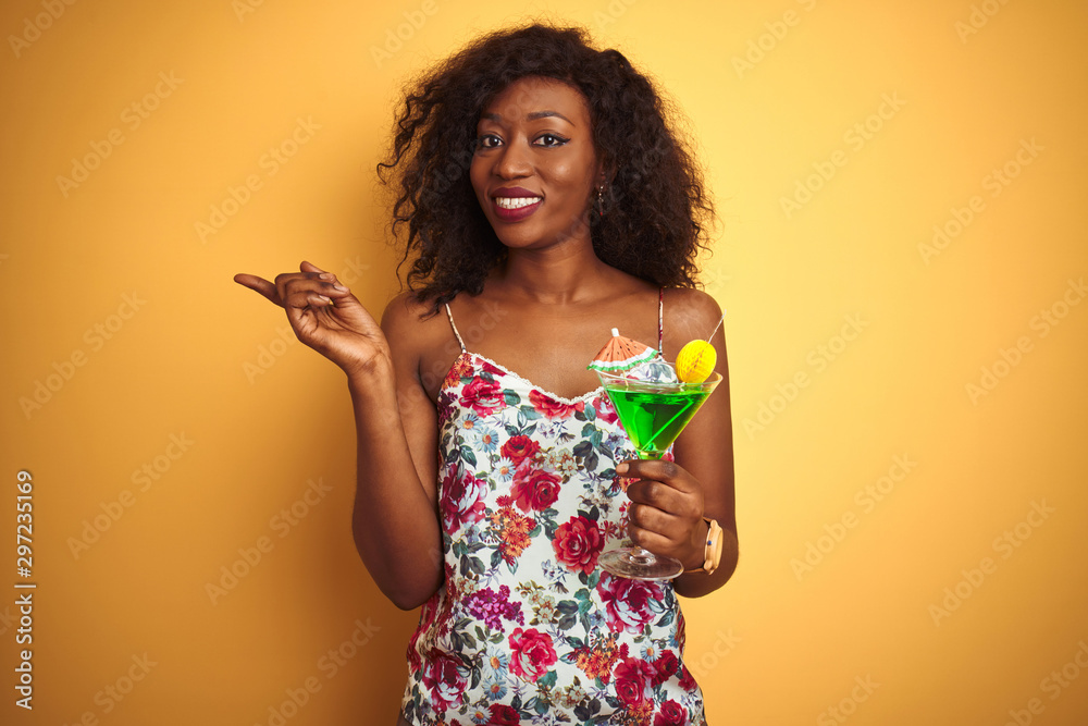 Young african american woman drinking cocktail standing over isolated yellow background very happy pointing with hand and finger to the side Young african american woman drinking cocktail standing over isolated yellow background very happy pointing with hand and finger to the side