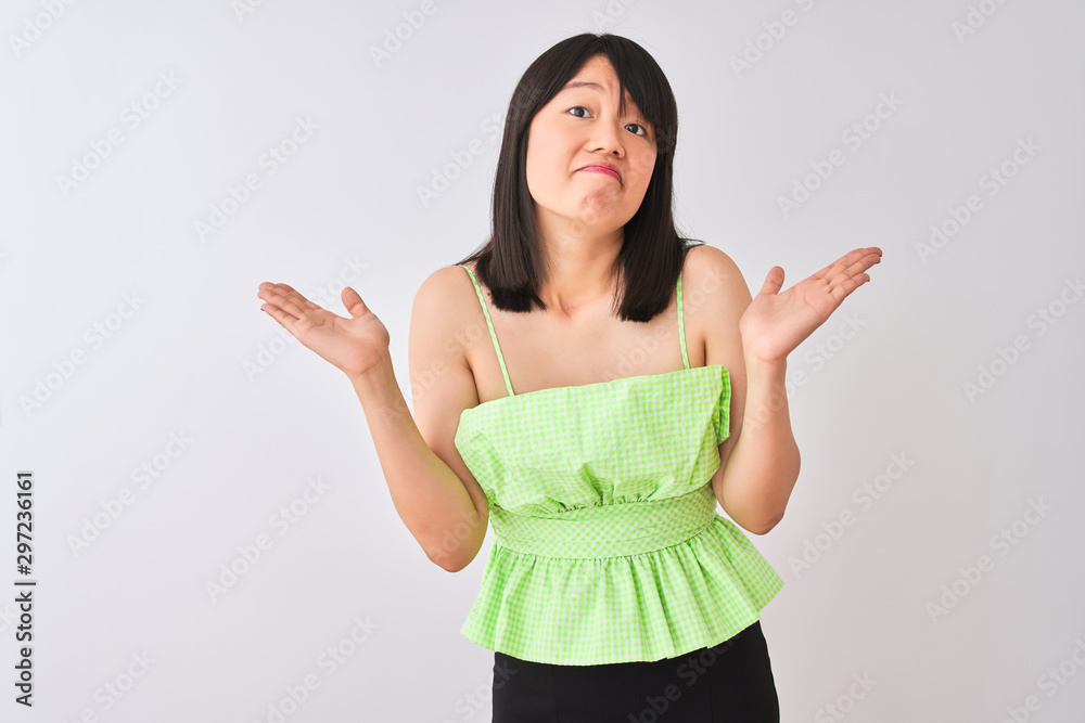 Young beautiful chinese woman wearing green t-shirt over isolated white background clueless and confused expression with arms and hands raised. Doubt concept. Young beautiful chinese woman wearing green t-shirt over isolated white background clueless and confused expression with arms and hands raised. Doubt concept.