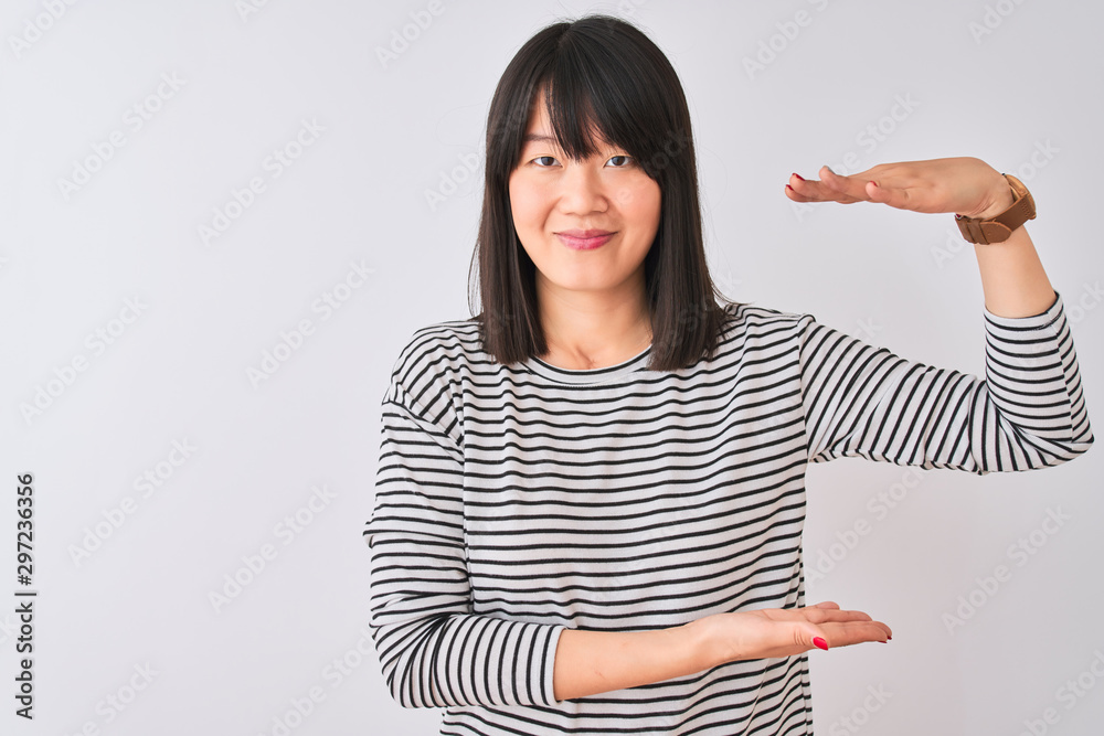 Young beautiful chinese woman wearing black striped t-shirt over isolated white background gesturing with hands showing big and large size sign, measure symbol. Smiling looking at the camera Young beautiful chinese woman wearing black striped t-shirt over isolated white background gesturing with hands showing big and large size sign, measure symbol. Smiling looking at the camera