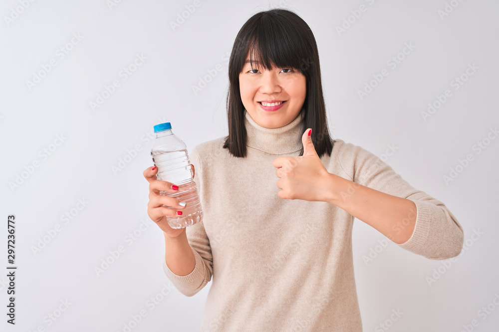 Young beautiful Chinese woman holding bottle of water over isolated white background happy with big smile doing ok sign, thumb up with fingers, excellent sign