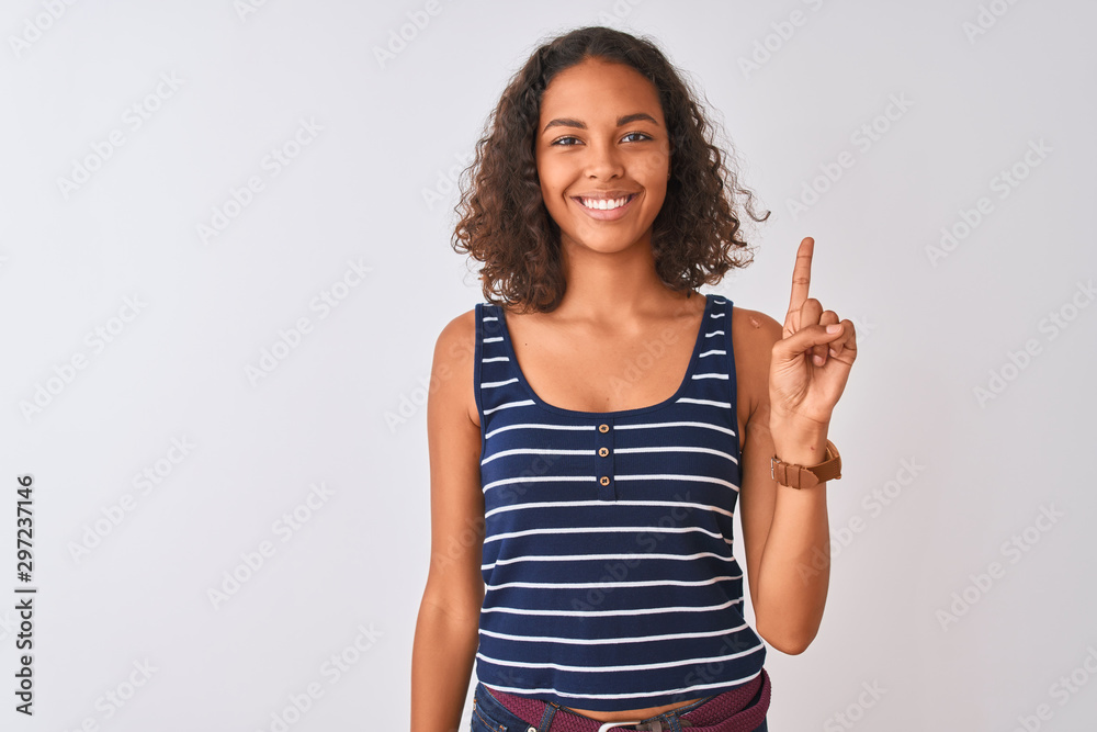 Young brazilian woman wearing striped t-shirt standing over isolated white background showing and pointing up with finger number one while smiling confident and happy. Young brazilian woman wearing striped t-shirt standing over isolated white background showing and pointing up with finger number one while smiling confident and happy.