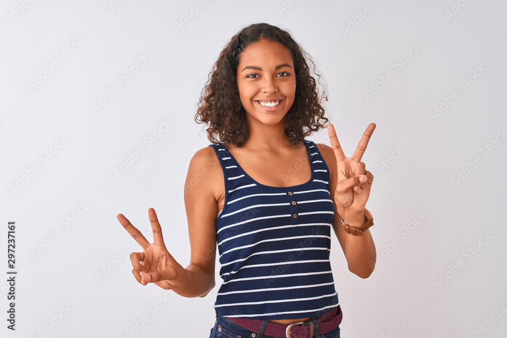 Young brazilian woman wearing striped t-shirt standing over isolated white background smiling looking to the camera showing fingers doing victory sign. Number two. Young brazilian woman wearing striped t-shirt standing over isolated white background smiling looking to the camera showing fingers doing victory sign. Number two.