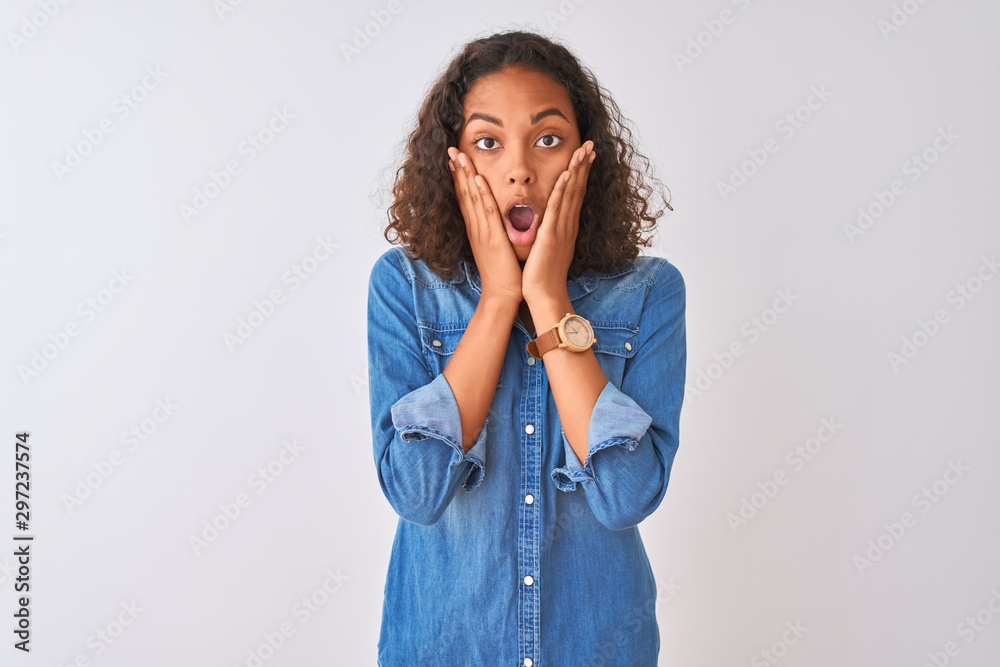 Young brazilian woman wearing denim shirt standing over isolated white background afraid and shocked, surprise and amazed expression with hands on face Young brazilian woman wearing denim shirt standing over isolated white background afraid and shocked, surprise and amazed expression with hands on face