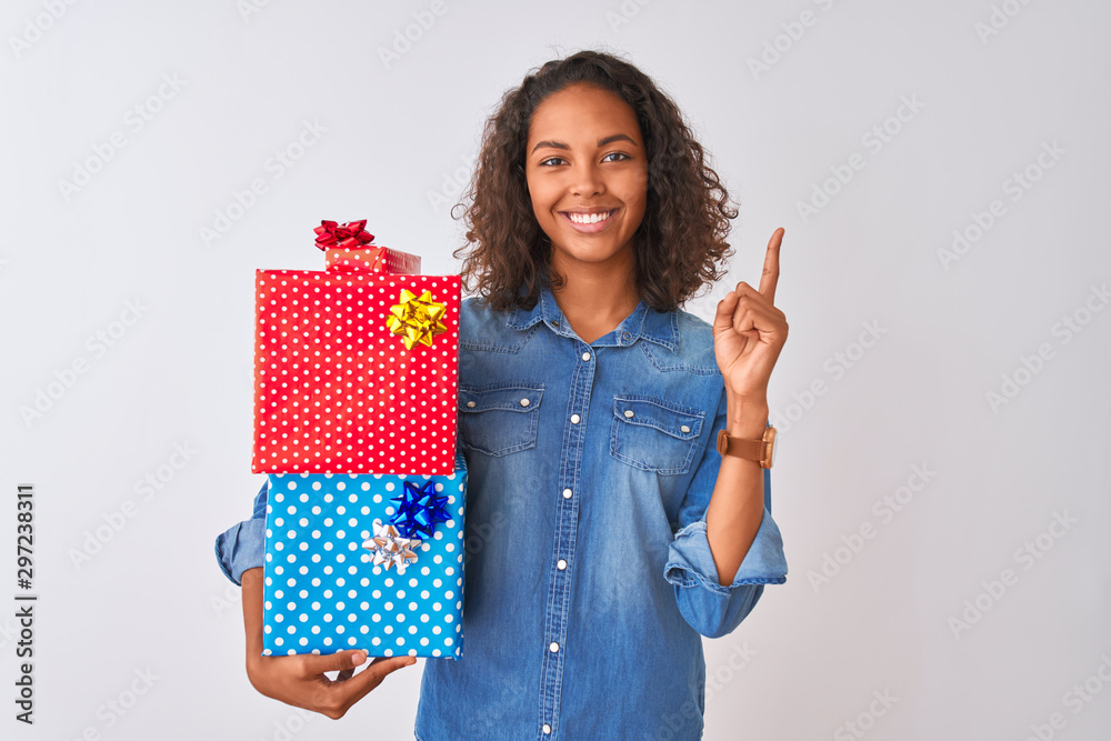Young brazilian woman holding birthday gifts standing over isolated white background surprised with an idea or question pointing finger with happy face, number one Young brazilian woman holding birthday gifts standing over isolated white background surprised with an idea or question pointing finger with happy face, number one