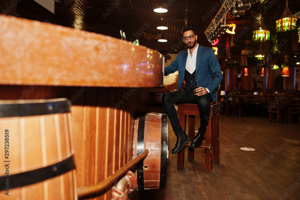 Handsome well-dressed arabian man with glass of whiskey and cigar posed at pub. Handsome well-dressed arabian man with glass of whiskey and cigar posed at pub.